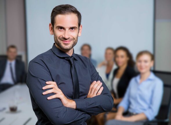 man-smiling-with-suit-sitting-table-with-colleagues (1)