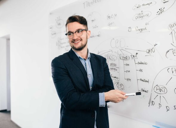 young-attractive-dark-haired-man-glasses-is-showing-business-plan-whiteboard-he-wears-blue-shirt-dark-jacket-he-is-smiling-side (1)